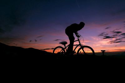 Silhouette man riding bicycle against sky during sunset