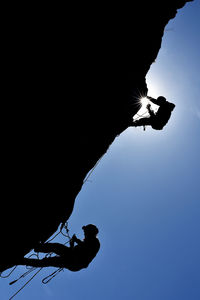 Low angle view of rock climbers against clear sky