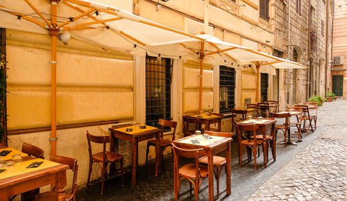 Empty chairs and tables at sidewalk cafe amidst buildings