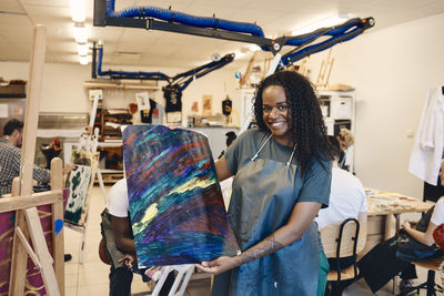 Portrait of happy woman with curly hair showing painting in art class