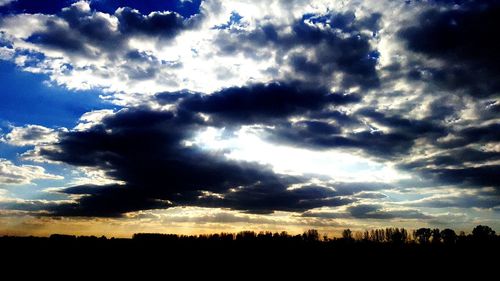 Low angle view of silhouette trees against dramatic sky