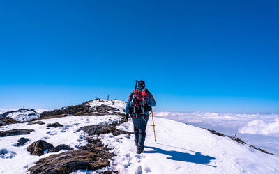 Rear view of man skiing on snowcapped mountain against clear blue sky