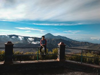 Man standing by railing on mountain against sky