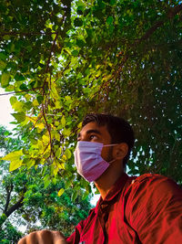 Portrait of young man looking away while standing against tree