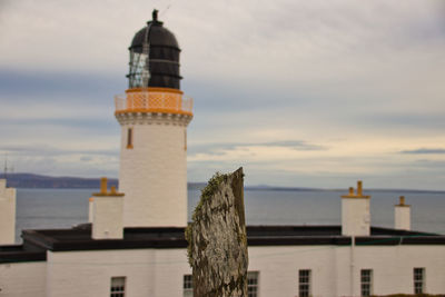 Lighthouse by building against sky