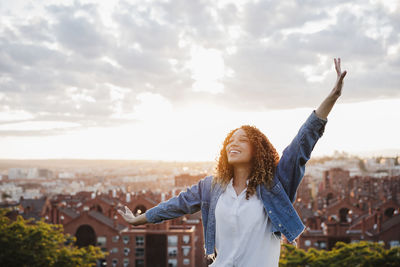 Young woman with arms outstretched standing against cityscape