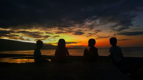 Silhouette friends at beach against sky during sunset