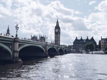 Bridge over river in city against cloudy sky