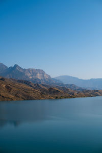 Scenic view of sea and mountains against clear blue sky