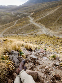 Low section of man sitting against winding roads on mountains