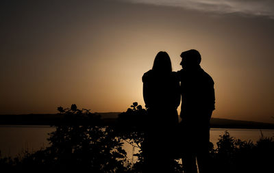 Rear view of silhouette couple overlooking calm lake