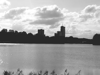 Calm river with buildings against cloudy sky