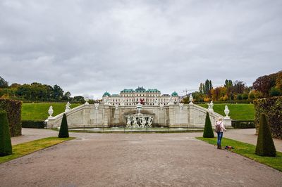 People on footpath in park against cloudy sky