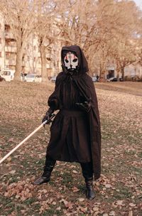 Full length of young man in halloween costume standing against bare trees during autumn