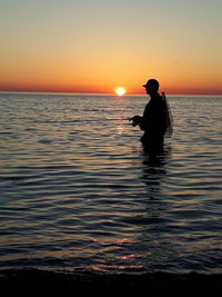 Silhouette man standing in sea against orange sky