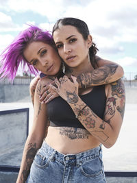 Female friends with eccentric appearance and tattoos embracing on street and looking at camera