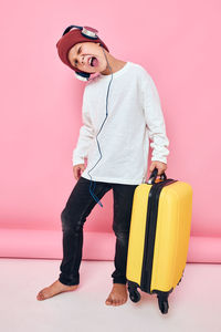 Portrait of young woman with suitcase against pink background