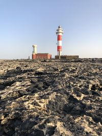 Lighthouse on beach by sea against clear sky