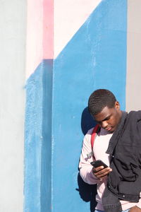 Young man using mobile phone while leaning on wall