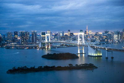 Illuminated bridge over river against sky in city