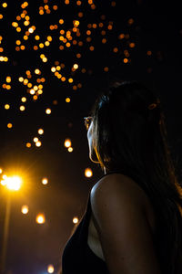 Side view of woman standing against lights at night