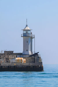 Lighthouse by sea against clear sky