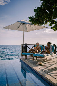 People sitting by swimming pool against sky