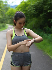 Young woman checking time while standing on road