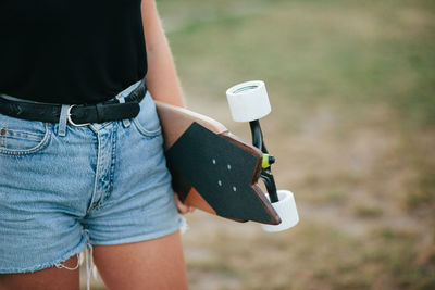 Midsection of woman holding skateboard while standing on field