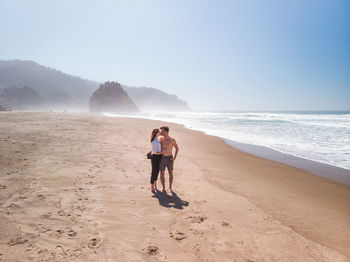 Couple kissing while standing at beach against sky