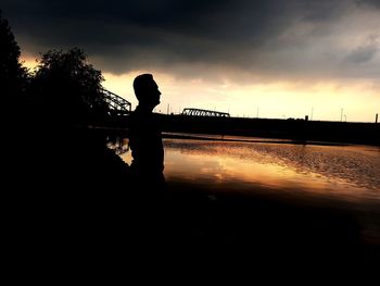 Silhouette man standing on bridge over river against sky