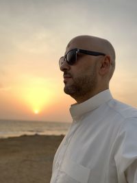 Portrait of man wearing sunglasses standing at beach during sunset