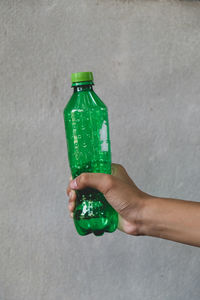 Close-up of hand holding bottle against wall