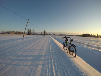 Bicycle on snow covered field against clear sky