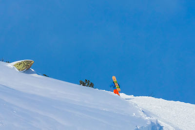 Man with snowboard walking on snow covered land against sky