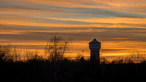 Silhouette tower and trees against orange sky