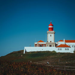 Lighthouse by sea against clear blue sky