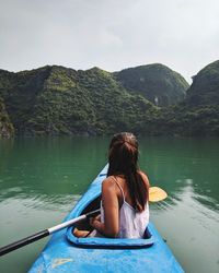 Rear view of woman kayaking on lake against mountains