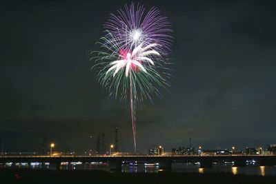 Bridge over river against firework display in sky at night