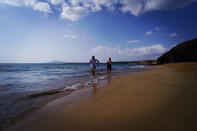Couple running on shore at beach against sky