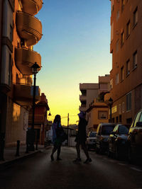 People walking on street amidst buildings in city during sunset