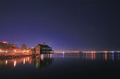 Illuminated buildings by lake against sky at night