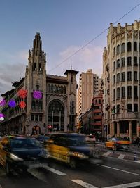 Cars on road by buildings against sky in city