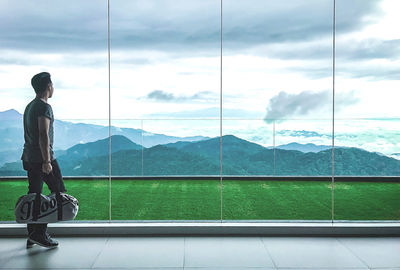Side view of man on glass window against sky