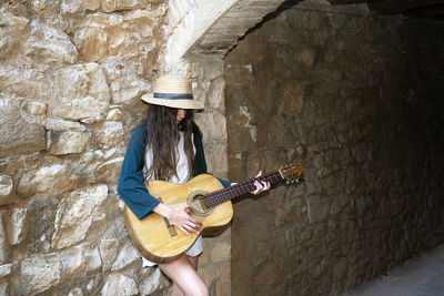 Woman playing guitar against wall