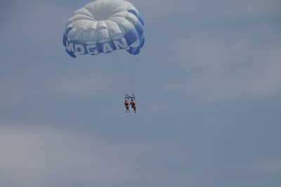 Low angle view of people paragliding against sky