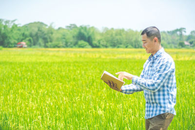 Side view of young man holding book on field