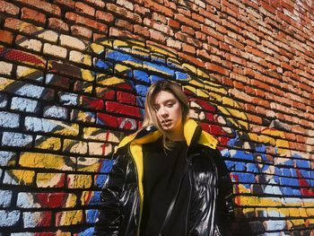 Portrait of young woman standing against brick wall