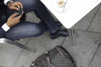 High angle low section of businessman using phone while sitting at sidewalk cafe