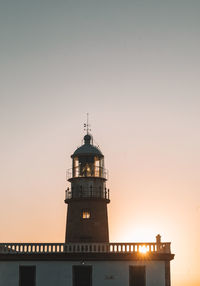 Lighthouse by sea against clear sky during sunset